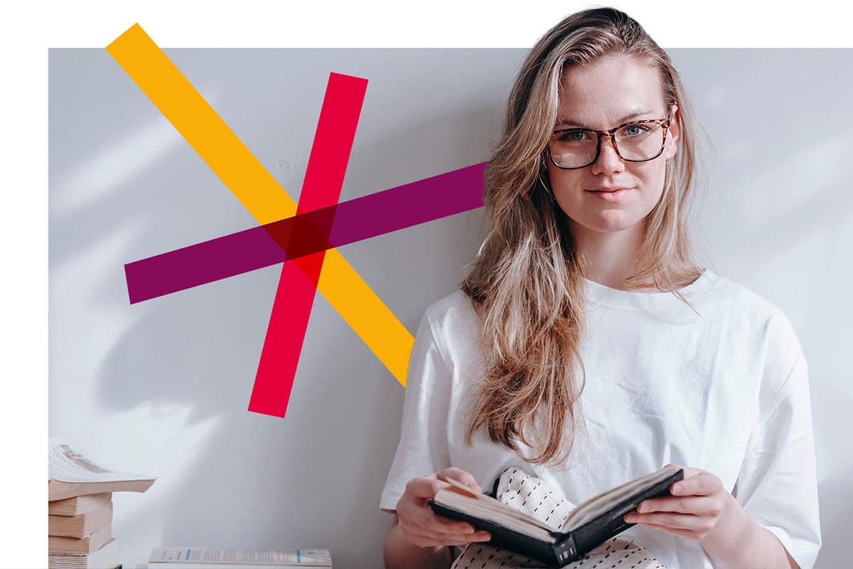 Woman with glasses smiling into the camera while holding a book